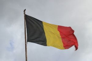 Belgische Nationalflagge wehend vor bewölktem Himmel.