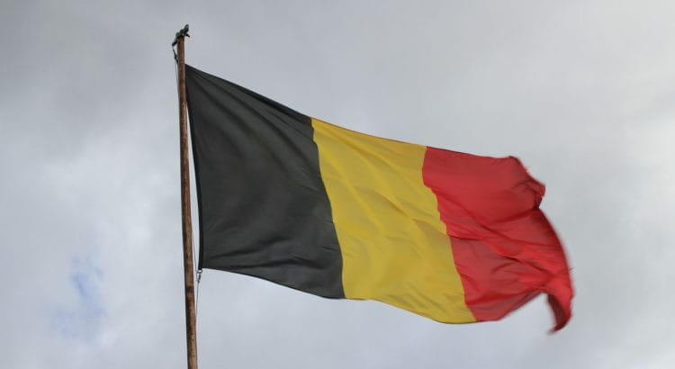 Belgische Nationalflagge wehend vor bewölktem Himmel.