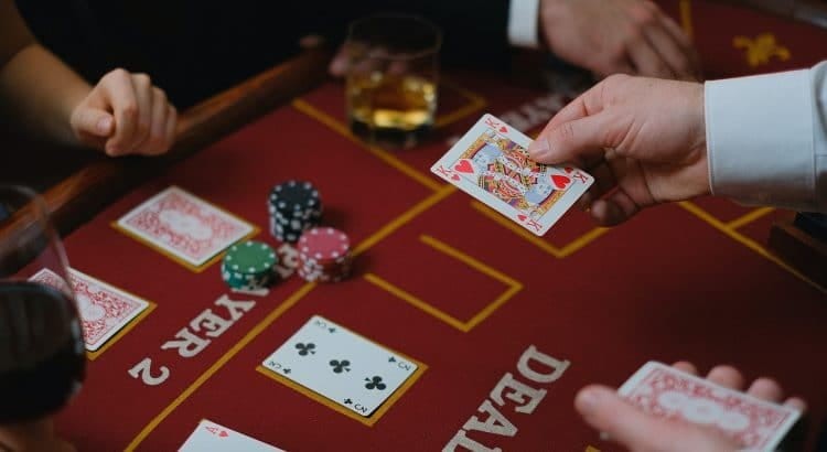 Eine Hand hält eine Spielkarte über einem Blackjack Tisch.