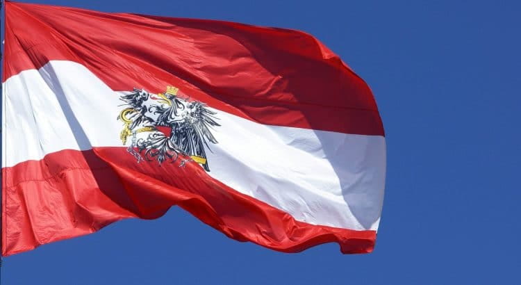 Österreichische Flagge wehend im Wind vor blauem Himmel.