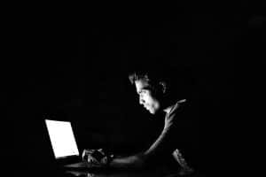 Junger Mann sitzt im Dunkeln vor einem Notebook.