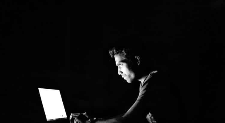Junger Mann sitzt im Dunkeln vor einem Notebook.