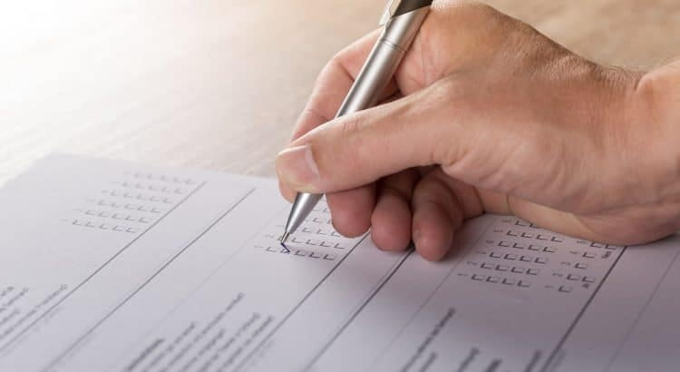 Hand mit Stift kreuzt Kästchen auf einem Fragebogen an.