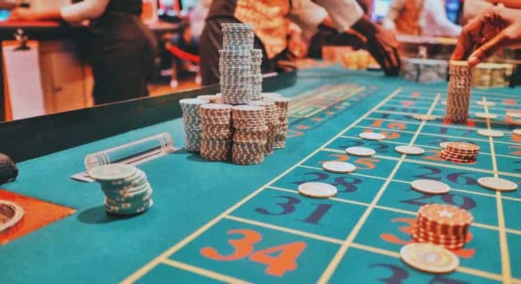 Zahlreiche gestapelte Jetons auf einem Roulette-Tisch eines Casinos; herum viele Spieler und Dealer aktiv.