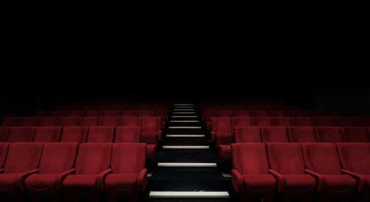 Zahlreiche leere rote Kinosessel in verdunkeltem Kinosaal.