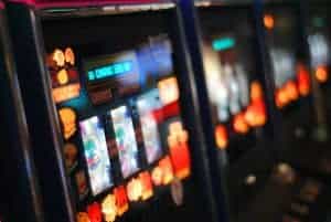 Ein Slot Game steht neben anderen Automatenspielen und leuchtet und vielen bunten Farben im dunklen Saal.