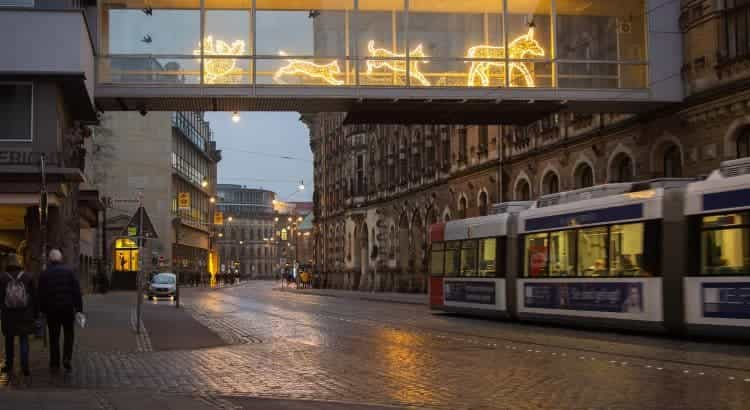 In Bremen laufen verschiedene Personen an einem verregneten Abend durch die Innenstadt, während eine S-Bahn vorbeifährt.