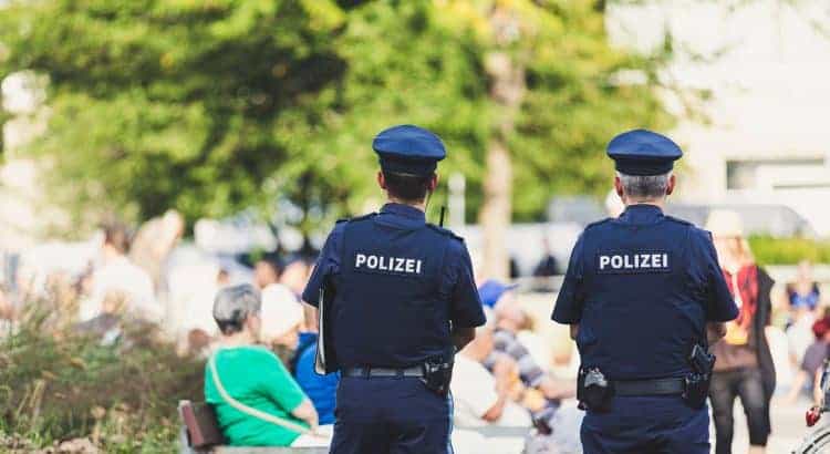 Zwei ältere männliche deutsche Polizisten in Uniform stehen mit dem Rücken zur Kamera gedreht in einer Stadt inmitten von Menschen