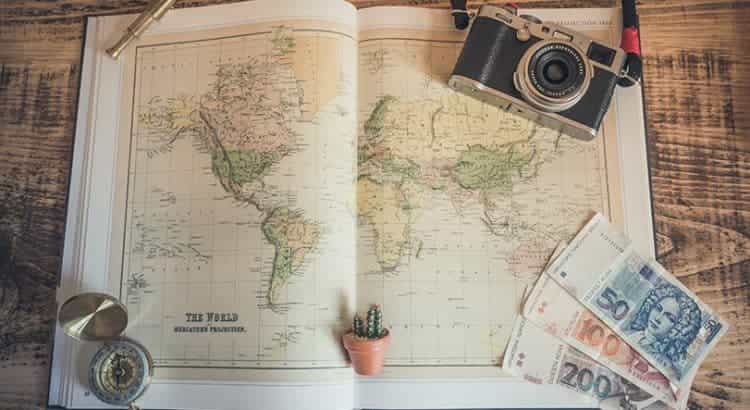 Ein aufgeschlagener Atlas mit unterschiedlichen Reiseutensilien daneben auf einem Tisch liegend.