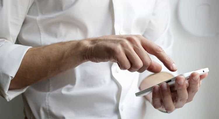 Ein Mann im weißen Hemd und hochgekrempelten Ärmeln tippt auf einem Smartphone.