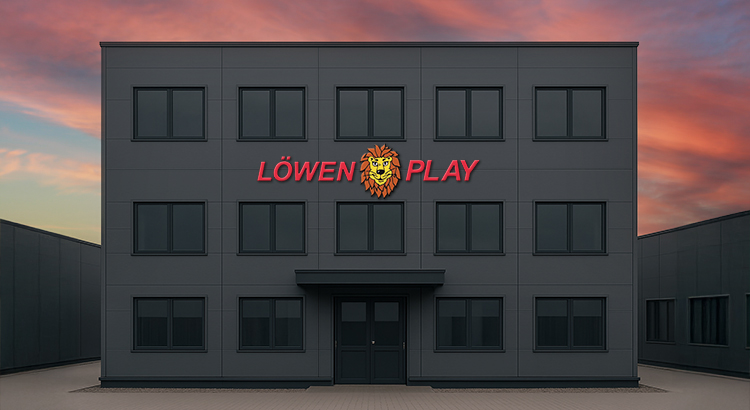 Außenansicht eines modernen Gebäudes von Löwen Play mit einem auffälligen roten Logo und einem Löwenkopf-Symbol, das an der Wand über der Eingangstür prangt. Das Gebäude ist in Grau gehalten und hebt sich vom grauen Himmel ab.