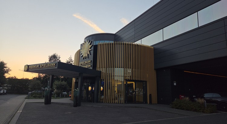 Eingang der Merkur Spielbank Monheim mit goldener Sonne und Vordach in der Abenddämmerung