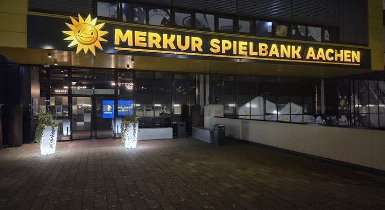 Beleuchteter Eingang der Merkur Spielbank Aachen am Tivoli-Stadion bei Nacht mit Sonnen-Logo und Schriftzug