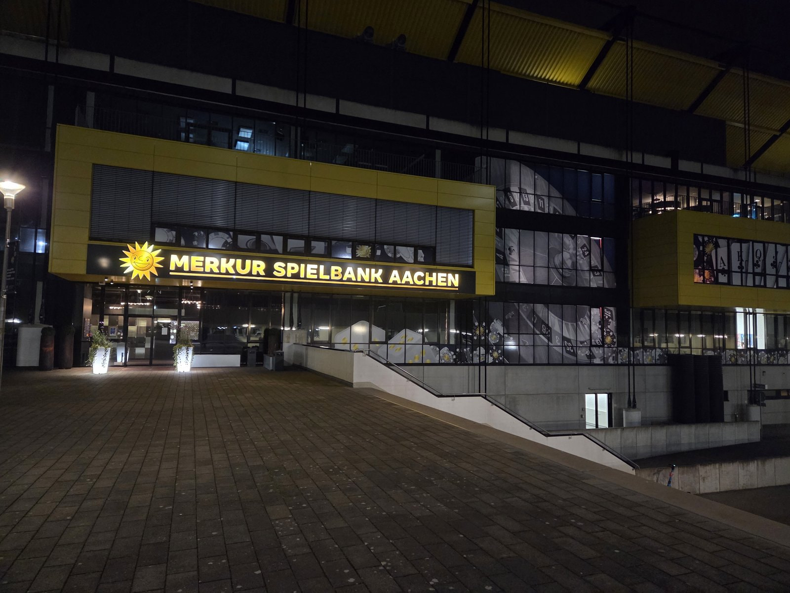 Merkur Spielbank Aachen bei Nacht mit leuchtendem Schriftzug über dem Eingang