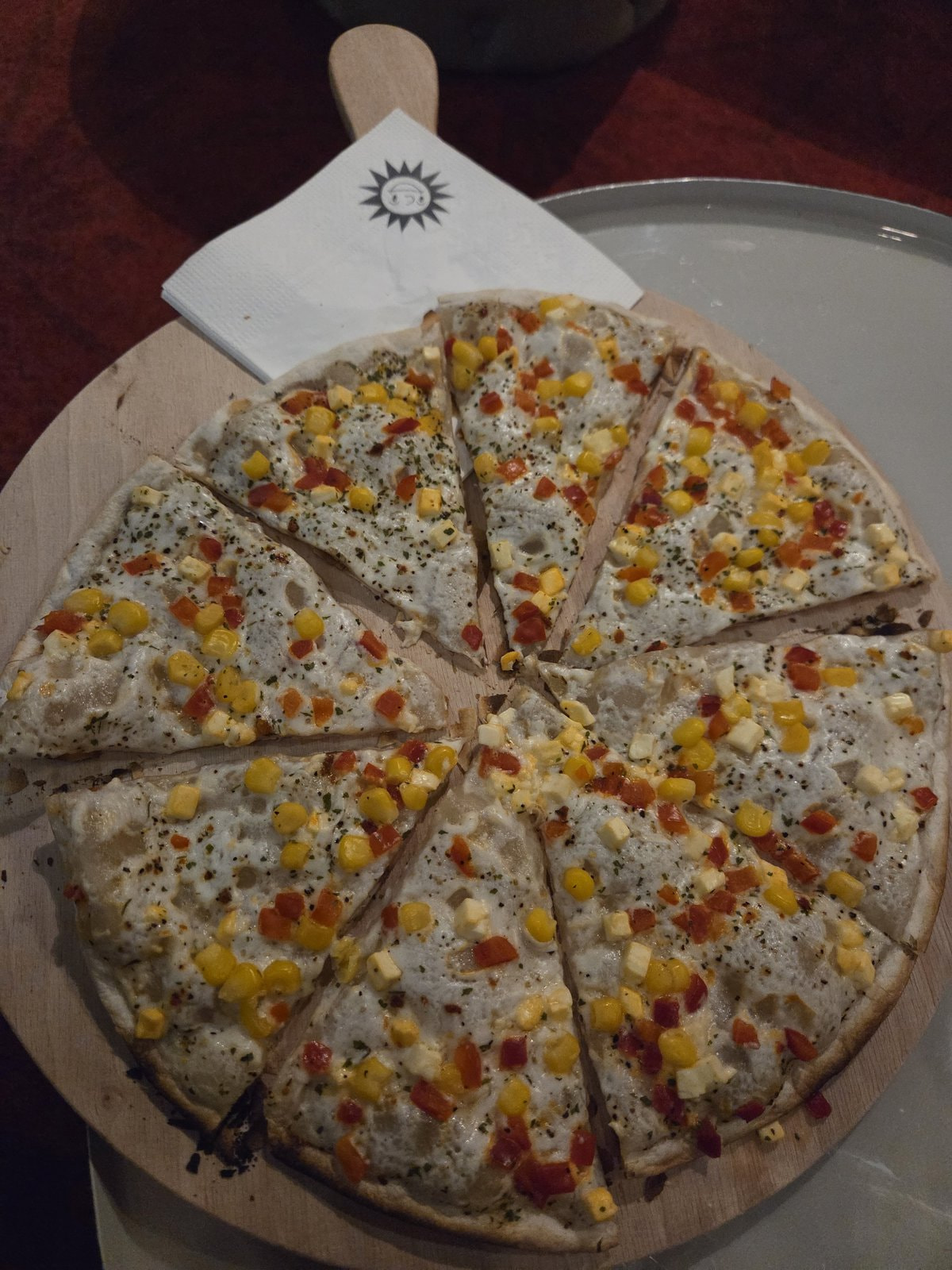 Flammkuchen mit Mais und Paprika auf einem Holzbrett mit Merkur-Logo