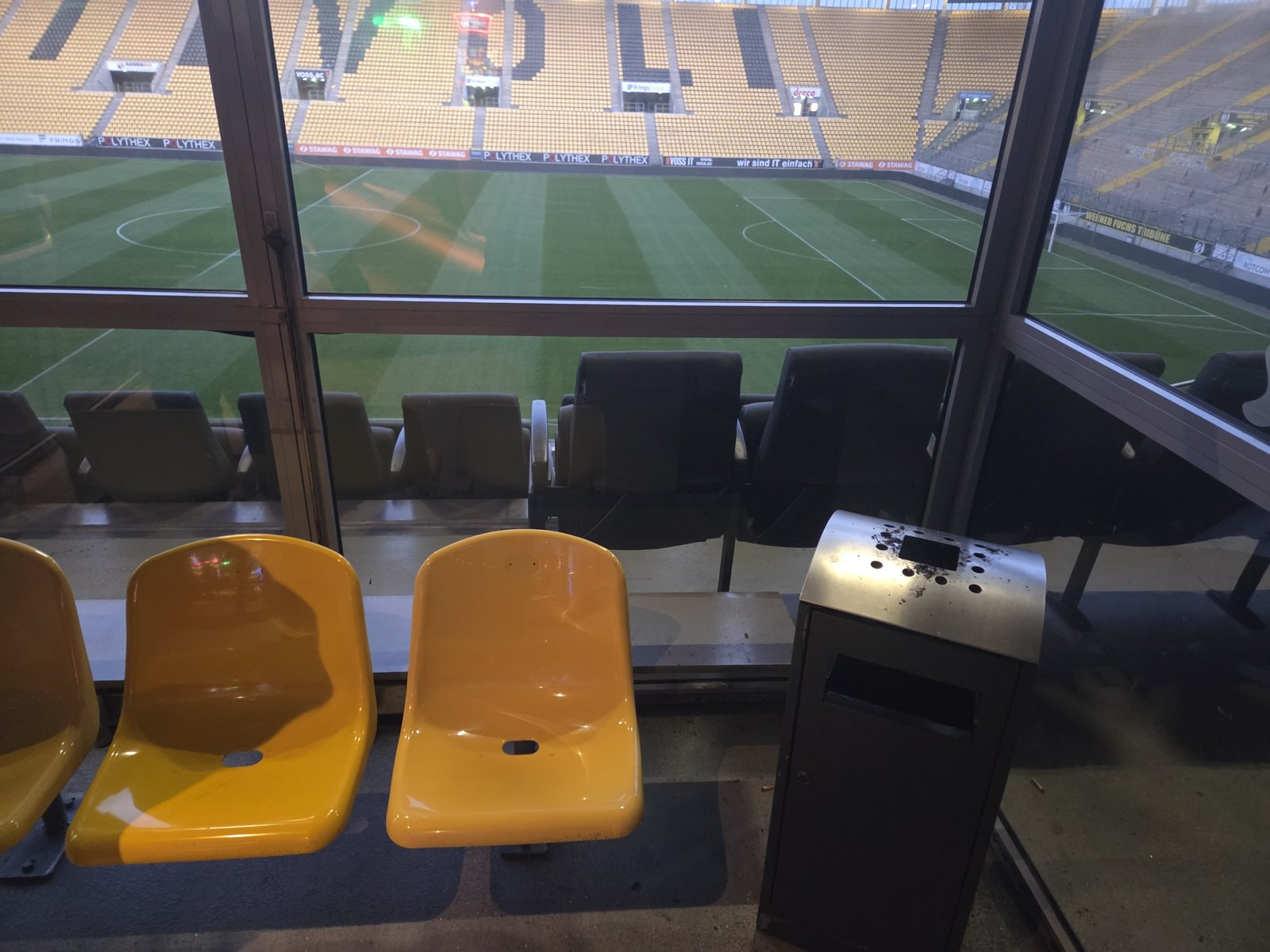 Gelbe Stadionsitze und Aschenbecher im Raucherbereich vor der Glasscheibe