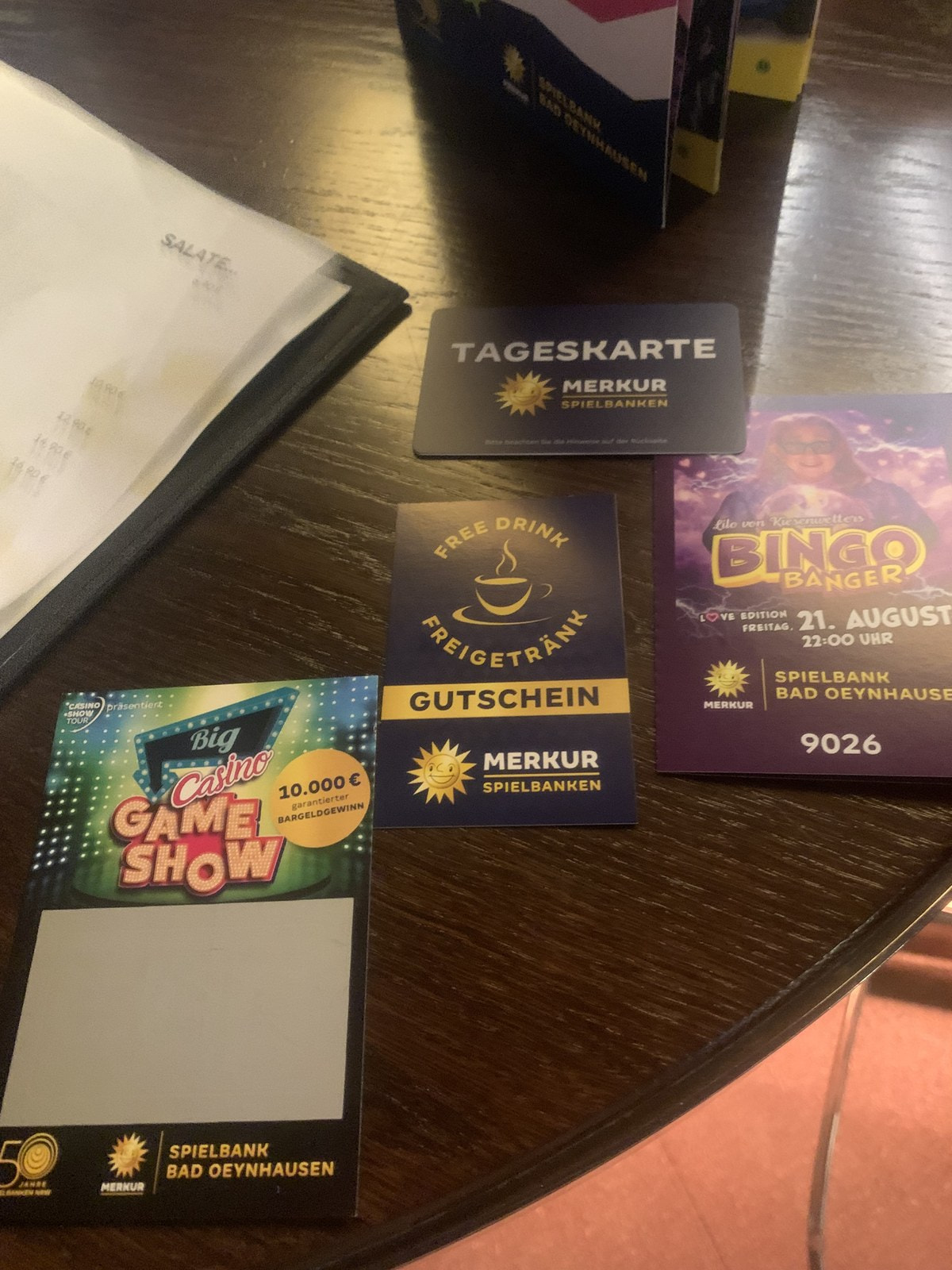 Tageskarte, Gutschein für ein Freigetränk und Veranstaltungsflyer der Spielbank Bad Oeynhausen auf einem Tisch